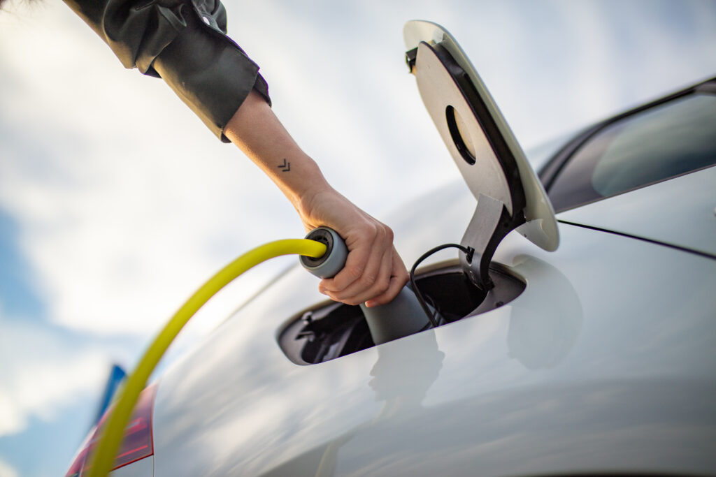 Low angle close-up shot of the hand of a woman holding a charging plug while charging an electric car at a charging station